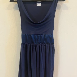 Mörkblå ärmlös topp med knyt i midjan - Säljer en mörkblå ärmlös topp med snygg drapering vid halsen och knytband i midjan. Toppen har en lös passform nedtill och är perfekt för en stilren look. Passar till både jeans och kjol.