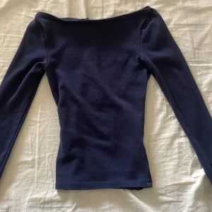 Mörkblå långärmad topp med bred halsringning - Säljer en mörkblå långärmad topp med bred, nästan båtringad hals. Modellen är tight och materialet känns mjukt och stretchigt, perfekt för en stilren look. Passar dig som gillar enkla men snygga basplagg.