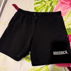 Svarta shorts från Hoodrich - Svarta shorts från Hoodrich med vit logga på vänster ben. De har snörning i midjan och är tillverkade i ett mjukt material som passar perfekt för sommar