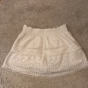 Vit broderad kortkjol med volang - Supersöt vit kortkjol med broderade blommor och volangdetaljer. Kjolen har resår i midjan och är perfekt för en somrig look. Lätt och luftig med fina spetsinslag och broderade mönster.Kjolen har också shorts inuti kjolen som inte syns. Perfekt nu till sommaren!