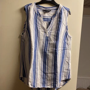 Randigt linne från Lindex - En ärmlös topp från Lindex i vitt och blått. Toppen har en v-ringad hals och är tillverkad i ett mjukt bomullsmaterial, perfekt för sommaren som snart närmar sig💕