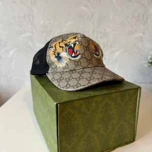 Gucci keps med tigerbrodyr - Vill få sålt så pris går att sänka❗️skriv till mig så sänks priset stort‼️‼️Snygg keps från Gucci med klassiskt GG-mönster i beige och brunt. Framtill finns broderade tigrar i gult, svart och rött. Baksidan är i svart mesh för extra ventilation. Perfekt accessoar för en trendig look.
