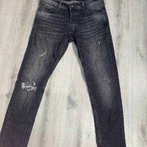 Svarta slitna jeans Jack&Jones  - Snygga svarta jeans med slitningar och hål på vänster ben. Riktigt fräscha Jack & Jones jeans. Perfekta för en trendig och avslappnad stil.
