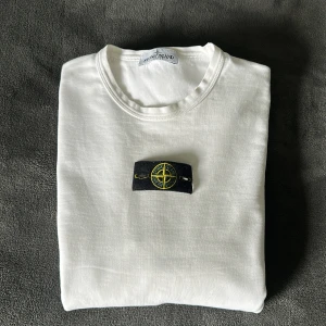 Vit långärmad tröja från Stone Island - Säljer en stilren vit långärmad tröja från Stone Island med den klassiska logotypen på armen. Tröjan har rund halsringning och är tillverkad i mjukt material. Vid frågor tveka inte på att höra av dig!