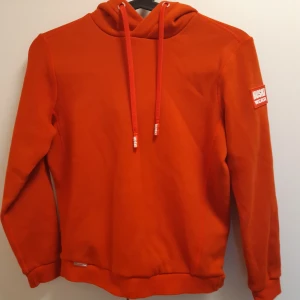Orange/röd hoodie från Huski Wear - Säljer en orange/röd hoodie från Huski Wear i juniorstorlek 134-140. Jätteduktig material! Knappt använd.