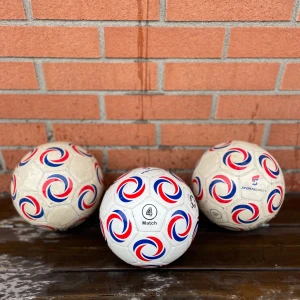 3 St Vita fotbollar med rödblått mönster - Säljer tre klassiska vita fotbollar med snygga röda och blå snurrmönster. Bollarna har storlek 4 och är märkt med 'Match'. Perfekt för träning eller matchspel på planen.