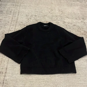 Svart stickad tröja från Gina Tricot - En svart stickad tröja från Gina Tricot i storlek XS. Tröjan har rund halsringning, långa ärmar och ribbade muddar vid ärmslut och nederkant. Perfekt baströja att matcha med det mesta. (Tvättas innan köp!)