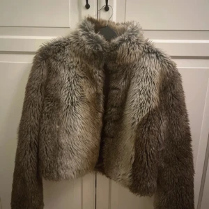 Brun pälsjacka från Sisters - Säljer en snygg brun pälsjacka från Sisters med hög krage och croppad passform. Jackan har långärmade ärmar och är tillverkad i akryl och polyester med mjukt foder. 