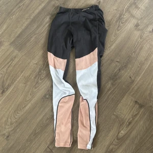 Flerfärgade leggings med paneler - Snygga leggings i svart, ljusrosa och ljusblått med coola paneldetaljer. Perfekta för dig som vill ha ett sportigt och trendigt plagg till träningen. Stretchigt material och hög komfort.