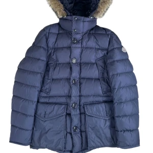Moncler Cluny  - Brand: Moncler   Modell: Cluny   Size: 2  Recomended fit: M  Condition: Very good besides inner cartoon is gone. (Picture 4)  Details:  Long parka with Real Coyote Fur. Has two pockets in the front, inner pocket. Both zip and buttons to close it with. Navy blue colorway. Available on Fashionels.com