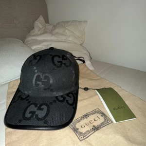 Svart keps från Gucci med GG-mönster - Snygg svart keps från Gucci med klassiskt GG-mönster i svart ton-i-ton. Justerbar rem baktill i läder och böjd skärm. Kepsen är tillverkad i ett mesh-liknande material och har märkets logga på insidan. dustbag tillkommer kepsen är i nystick med prislapp