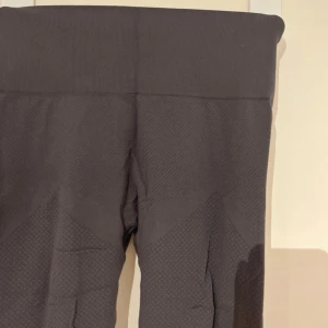 Mörkgrå sömlösa tights - Mörkgrå tights med hög midja och sömlös design. Byxorna har diskreta mönsterdetaljer längs benen och runt höfterna för en snygg look. Perfekta för träning eller en sportig vardagsstil.