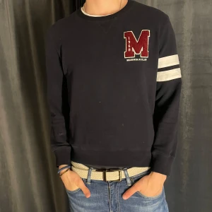 Mörkblå sweatshirt från Morris  - Säljer en mörkblå sweatshirt från Morris i storlek L. Tröjan har en stor röd M-logga på bröstet och två vita ränder på ena ärmen. Klassisk rund halsringning och mjukt bomullsmaterial. Den är liten i storleken. Skick 7/10✅ Pris kan diskuteras vid snabb affär💸