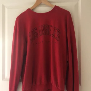 Röd sweatshirt med Los Angeles-tryck från SHEIN - Röd sweatshirt från SHEIN med trycket 'Los Angeles California' på bröstet. Klassisk rund halsringning och långa ärmar. Perfekt för en avslappnad stil.