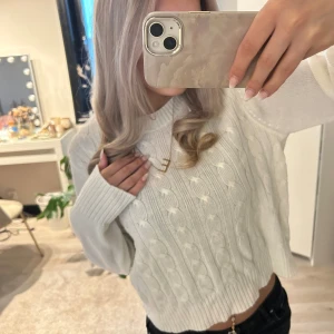 Vit stickad croppad tröja - Säljer en vit stickad croppad tröja med kabelstickat mönster och långa ärmar. Tröjan har en klassisk rund halsringning och ribbade muddar. Perfekt för lager-på-lager och enkel att matcha med jeans eller kjol.