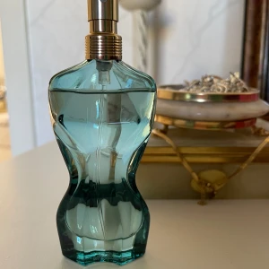 La Belle Paradise Garden Eau de Parfum - En parfym från Jean Paul Gaultier i en turkosgrön glasflaska formad som en kvinnokropp. Flaskan har guldigt spraymunstycke och detaljer. Doften heter La Belle Paradise Garden och är känd för sin fräscha och blommiga karaktär.