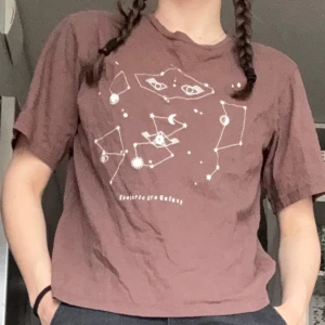 Brun t-shirt med galaxmotiv - OBS!! ALLA MINA PLAGG GRATIS VID UPPHÄTMNING I RÅCKSTA!!! En brun t-shirt med vitt tryck av stjärnbilder och galaxmotiv på framsidan. 