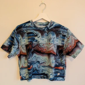 Fila - Cropped t-shirt I storlek M - T-shirt från Fila med unikt mönster och reflektiv logga i nedre kant. Något elastiskt material (bomull och elastan). Croppad modell. Från rökfritt och djurfritt hem.
