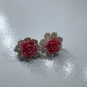 Rosa blomformade örhängen - Säljer ett par söta örhängen med rosformade detaljer i rosa och vita blad runt om. Perfekta för att ge en romantisk touch till din outfit. Passar dig som gillar unika accessoarer med blommig design.