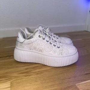 Vita sneakers från Karl Lagerfeld med platåsula - Säljer ett par vita sneakers från Karl Lagerfeld med hög platåsula och diskret mönster med loggor över hela skon. Skorna har snörning och rund tå, perfekta för dig som vill sticka ut lite extra. De är lite smutsiga på sidan men jag tror att det går att ta bort. Ena skosnöre är också lite smutsig men det är lätt att byta ut. De köptes för 2000kr om inte mer