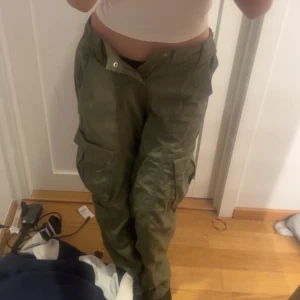 Gröna cargopants med fickor - Säljer ett par gröna cargopants med flera stora fickor på sidorna och resår vid bensluten. Byxorna har en loose passform och är perfekta för en avslappnad stil.