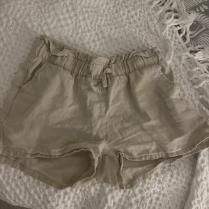 Beiga linneshorts med knytband - Säljer ett par beiga shorts i linne med knytband framtill. Shortsen har två sidofickor och en avslappnad passform, perfekta för varma dagar.