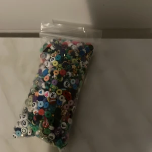 Påse med färgglada pärlor och bokstavspärlor - En påse fylld med blandade färgglada pärlor och bokstavspärlor, perfekta för att skapa egna armband, halsband eller andra smycken. Pärlorna kommer i olika former och färger för kreativt pyssel.