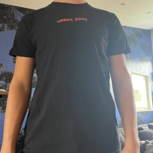 Svart t-shirt - Svart t-shirt från Urban Edge med röd text på bröstet och stort färgglatt tryck på ryggen. T-shirten har en klassisk passform och är tillverkad i mjuk bomull. Perfekt för en cool och avslappnad stil. Storlek M och normal i passform, mkt bra skick! 🤩👍🏼