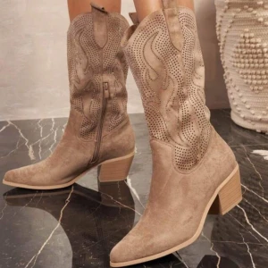 Beige cowboy boots med perforerat mönster - Säljer ett par snygga beige cowboy boots med perforerat mönster och dekorativa detaljer på skaftet. Skorna har spetsig tå, klack och dragkedja på sidan. Perfekta för dig som vill sticka ut med en western-inspirerad look.
