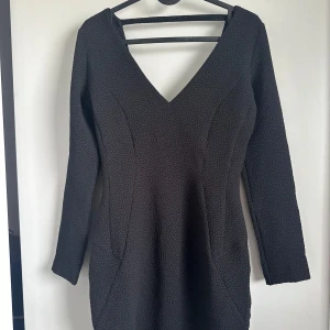 Svart klänning  - Säljer en svart långärmad klänning från Devier i storlek XS. Klänningen har v-ringning både fram och bak samt en figurnära passform. Materialet är strukturerat och ger en snygg look.