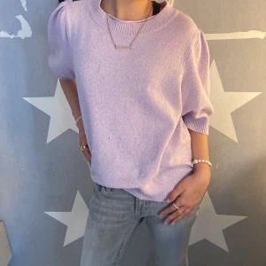 Ljuslila stickad tröja med puffärm - Superfin ljuslila stickad tröja med puffiga halvlånga ärmar och bred ribbad mudd vid hals, ärmslut och nederkant. Perfekt för en trendig och avslappnad look. Säljes i storlek M.