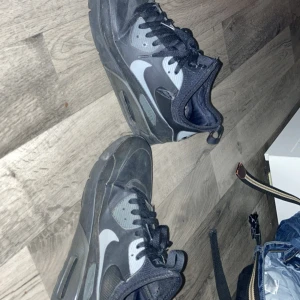 Svarta Nike Air Max sneakers - Säljer ett par svarta Nike Air Max sneakers med vit swoosh och svarta skosnören. Skorna har en sportig design med rund tå och platt sula, perfekta för vardagsstil. Klassisk Air Max-dämpning i sulan för extra komfort.