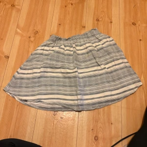 Randig kjol från Pieces - Kort kjol från Pieces i vitt och ljusblått med horisontella ränder. Kjolen har resår i midjan och är gjord i ett mjukt bomullsmaterial. Perfekt för varma dagar och enkel att matcha med olika toppar.