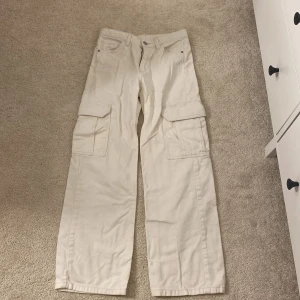 Beiga cargopants med raka ben - Säljer ett par beiga cargopants med raka ben och stora fickor på sidorna. Byxorna har normal passform och är perfekta för en avslappnad stil. Tillverkade i bomull för en skön känsla hela dagen.