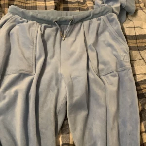 Ljusblå mjukisbyxor från Juicy Couture - Säljer ett par ljusblå mjukisbyxor från Juicy Couture med broderad logga på fickan och snörning i midjan. Byxorna har stora fickor med tryckknappar och är gjorda i ett mjukt, fleeceliknande material. Perfekta för en avslappnad stil, använt ca/2-3 gånger . Litet paket kommer de i❤️ kan tänka mej sänka pris vid snabbt köp 