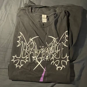 Band-tshirt Mayhem - Svart t-shirt med tryck från norska black metal-bandet Mayhem. Framsidan har bandets logga, kyrka i lila och texten 'De Mysteriis Dom Sathanas'. Baksidan har tre dödskallar och texten 'DSP'. Perfekt för metalheads!
