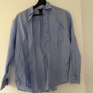 Ljusblå skjorta från Lindex - Klassisk ljusblå skjorta från Lindex i storlek S. Skjortan har långa ärmar, knappar framtill och klassisk krage. Perfekt för en stilren och enkel look. Tillverkad i mjukt material som känns skönt mot huden.