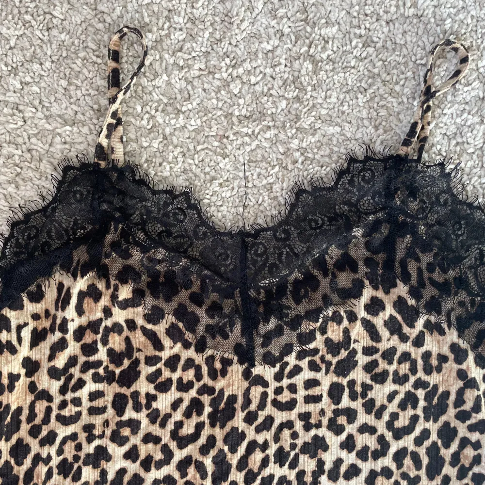 Säljer ett leopardmönstrat linne med tunna axelband och svart spets upptill. Toppen har en croppad passform och är perfekt för dig som vill sticka ut med ett djurmönster. Materialet känns mjukt och följsamt.. Yläosat.
