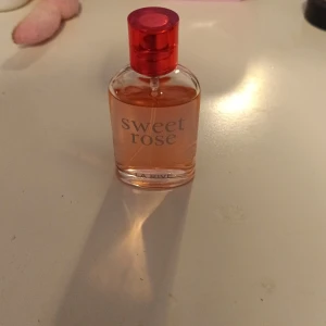 Sweet Rose parfym från La Rive - Säljer en söt parfym från La Rive med namnet Sweet Rose. Flaskan är genomskinlig med ljusrosa vätska och har ett rött lock. Doften är blommig och feminin, perfekt för dig som gillar rosor.
