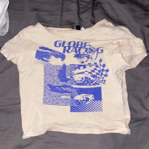 Beige t-shirt med blått tryck från H&M Divided - Säljer en beige t-shirt från H&M Divided med blått grafiskt tryck och texten 'Globe Racing' framtill. Säljer för den är för liten!🩷