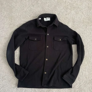 Svart overshirt från Selected Homme - Säljer en svart overshirt från Selected Homme med två bröstfickor och knappar framtill. Skjortan har lång ärm och är tillverkad i ett mjukt material som passar perfekt som lager över en t-shirt. Pris kan diskuteras.