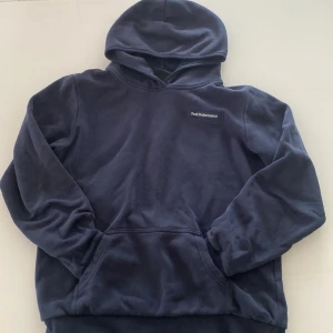 Mörkblå hoodie från Peak Performance - Mysig mörkblå hoodie från Peak Performance med broderad logga på bröstet. Tröjan har huva och en stor magficka framtill. Perfekt för kyliga dagar och enkel att matcha med det mesta.