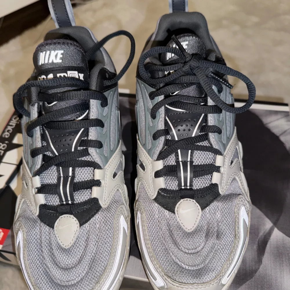 Nike Air Vapormax 360 sneakers i grått, svart och vitt med genomskinlig sula. Ovandelen är i mesh och syntet med svarta snören och silverdetaljer. Swoosh-logga på sidan och klassisk Vapormax-dämpning för en futuristisk look.. Kengät.