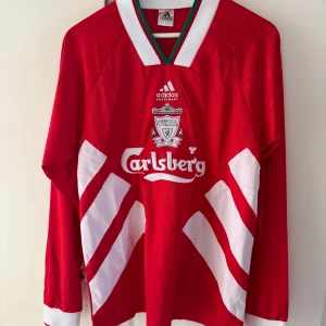 Liverpool retro vintage långärmad fotbollströja från Adidas - Klassisk röd Liverpool fotbollströja från Adidas med vita detaljer och Carlsberg-logga på bröstet. Långärmad modell i 100% polyester, tillverkad i Storbritannien. Perfekt för dig som älskar retrostil och fotboll. Passar storlek M inte be L.