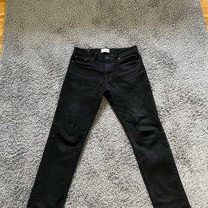 Svarta jeans från Jack & Jones - Snygga svarta jeans från Jack & Jones med en klassisk design. De har en normal passform och är perfekta för en stilren look. Jeansen har fem fickor och stängs med dragkedja och knapp storlek 30 30.