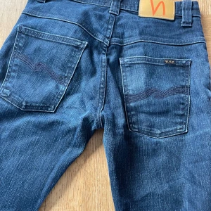 Mörkblå jeans från Nudie - Snygga mörkblå jeans från Nudie med klassisk femficksdesign och subtila slitningar. De har en rak passform och är tillverkade i högkvalitativt denim. Perfekta för en avslappnad stil.