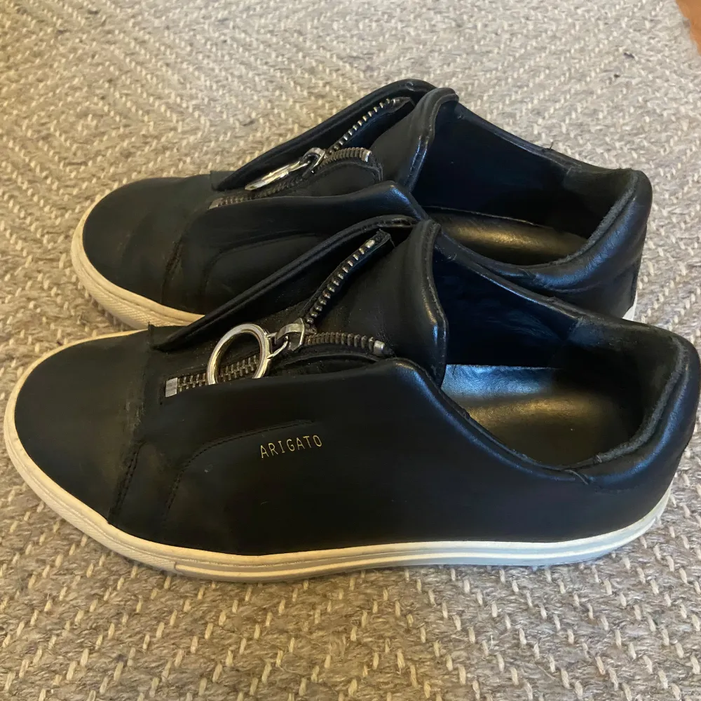 Säljer ett par svarta sneakers från Axel Arigato med unik dragkedjedetalj och ring framtill istället för klassisk snörning. Storlek 36. Kengät.
