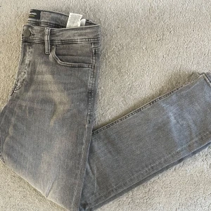 Gråa nya Jack and Jones jeans - Ett par mörkgråa jack and Jones jeans i modellen slim/glenn storlek 31/32. De är aldrig använda då de inte passade mig, men utan prislapp vilket drar ner priset. Nypris ligger på cirka 900, mitt pris 199! Hör av dig vid minsta fundering!