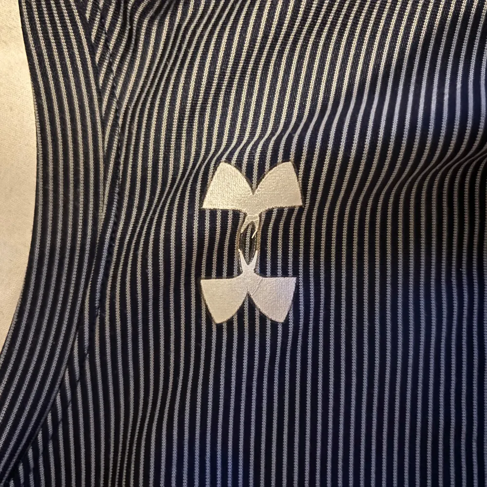 Säljer en svart och vit randig t-shirt från Under Armour med korta ärmar och löst passform. Perfekt för träning med HeatGear-material som håller dig sval. Klassisk logga på bröstet.. T-paidat.