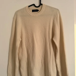 Beige stickad tröja från Riley - Säljer en beige stickad tröja från Riley. Tröjan har rund halsringning och lång ärm, med en grovstickad struktur som ger en avslappnad och stilren look. Perfekt för lager-på-lager under kyligare dagar.
